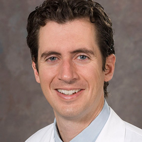 Man with brown curly hair wearing a white coat