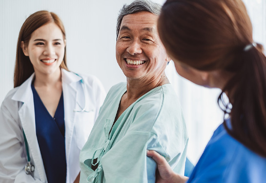 Male patient, center, in hospital gown smiles at nurse while doctor looks on