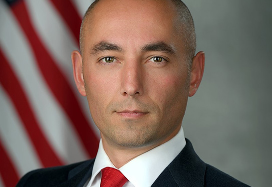 Man wearing a suit with an American flag behind him