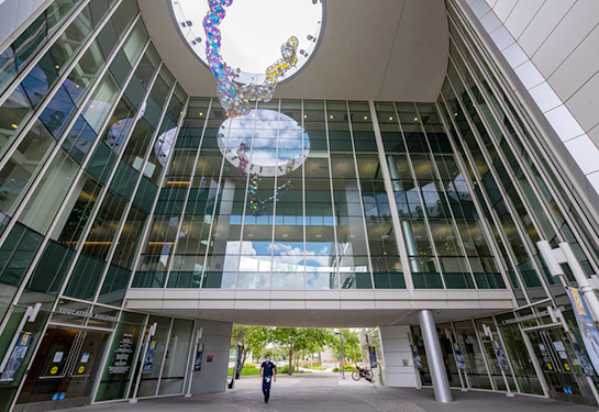 Building with glass windows and person wearing blue scrubs walking in front of the building