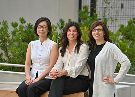 Two women sitting and one-woman standing side-by-side and smiling