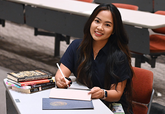 A young woman sits in a lecture hall next to medical school textbooks