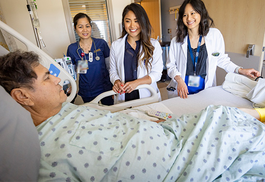 Two doctors and a nurse standing next to a male patient lying in hospital bed