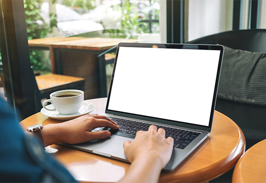 Person typing on a laptop with a cup of coffee to the left