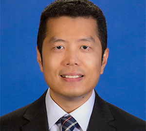 Man with dark hair wearing a suit smiling into camera.