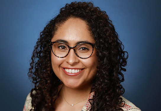 Portrait of woman wearing glasses and with dark, curly hair past her shoulders.