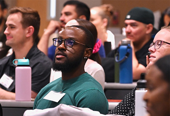 A group of medical students, male and female, sitting at long tables in lecture hall