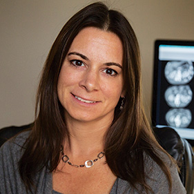 Woman with long brown hair in navy blue shirt smiling into camera.