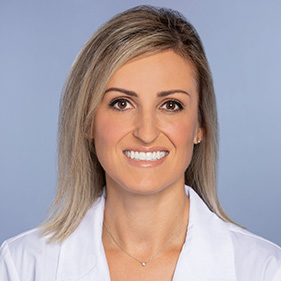 a woman with long blond hair wearing a white physician&rsquo;s jacket smiles for the camera.