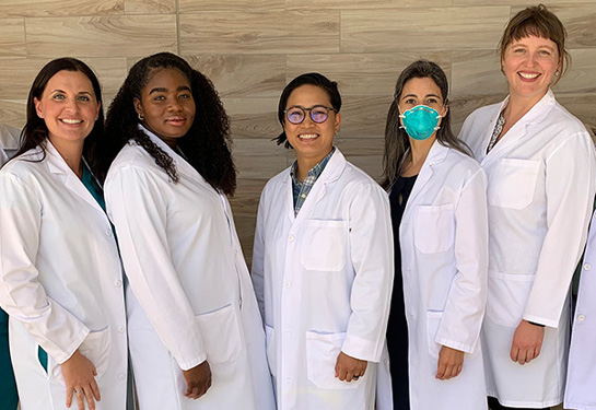 Clinicians in white coats stand in row smiling at camera