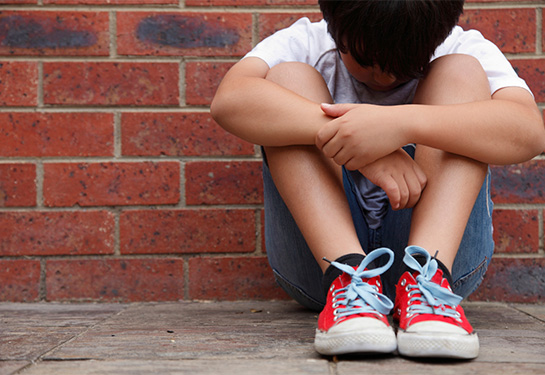 Child covers his face while sitting on the ground. 