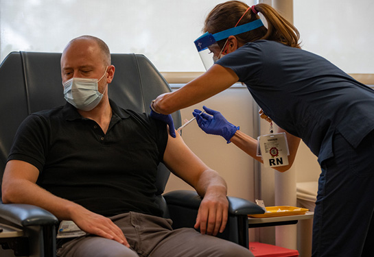 Man wearing black shirt sitting and receiving injection in arm