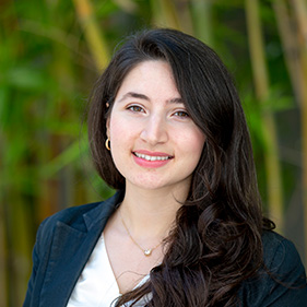 Woman in dark blazer and white blouse with dark, long hair smiling into camera