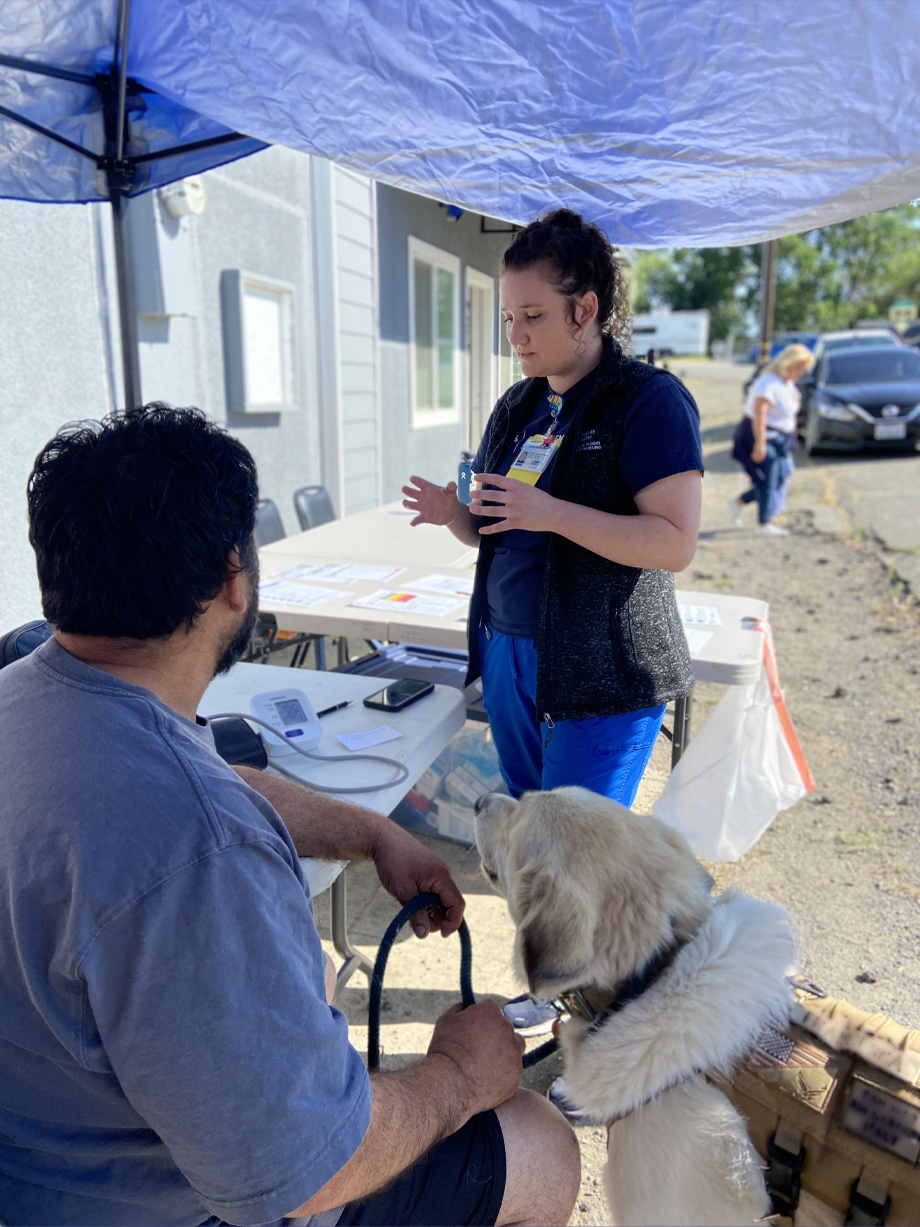 Nursing student talks to a man who is holding the leash of dog next to him