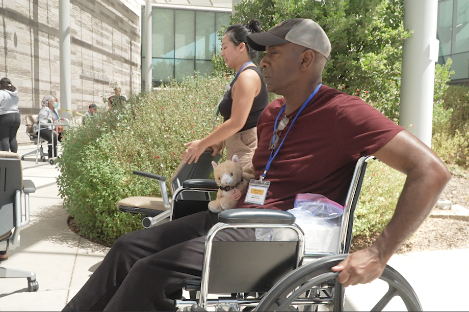 Man in maroon shirt in wheelchair holding cat stuffed animal