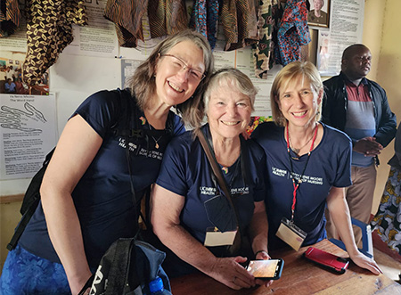 Three women wearing blue shirts, sitting and smiling together