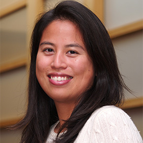 A woman with dark hair, wearing a white sweater smiles for a portrait