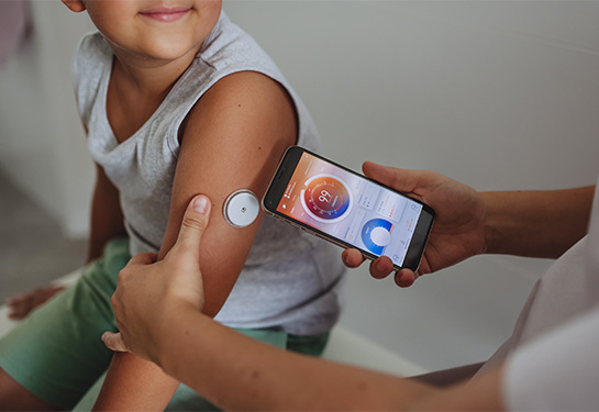 Boy with diabetes checks blood glucose level at home using continuous glucose monitor.