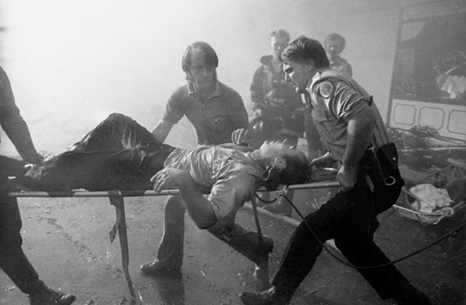  Two firefighters hurriedly carry an injured man lying on a stretcher while bystanders look on.