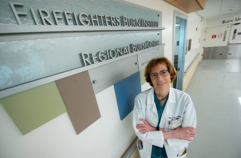  A woman wearing white doctor’s coat next to wall sign that reads: Firefighters Burn Institute Regional Burn Center.