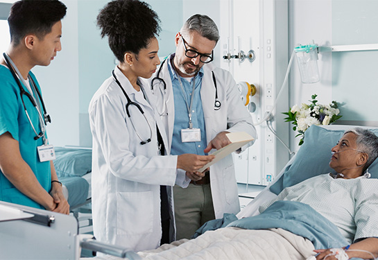 Woman with short hair laying in hospital bed looking at three medical professionals standing next to her while viewing a document