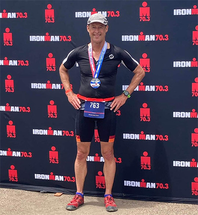 Man wearing medal around his neck standing in front of sign saying Iron Man Competition