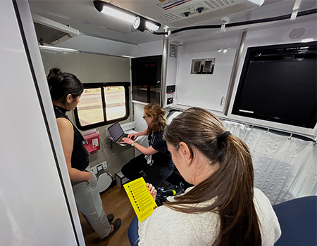 A woman stands and two women sit while chatting in the medical exam room of a mobile health clinic