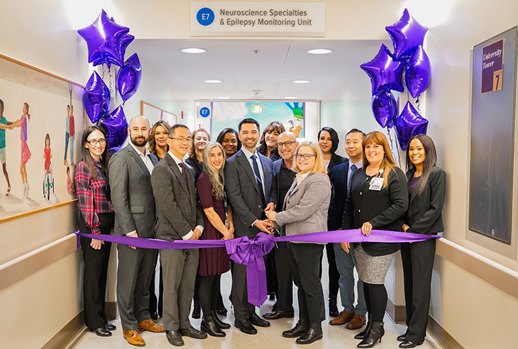 UC Davis Health leaders pose under the “Epilepsy Monitoring Unit” marquee with scissors and a purple ribbon.