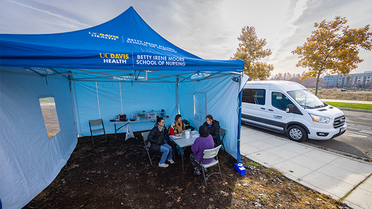 Four women seated around a table under a blue popup tent labeled “UC Davis Health Betty Irene Moore School of Nursing” 