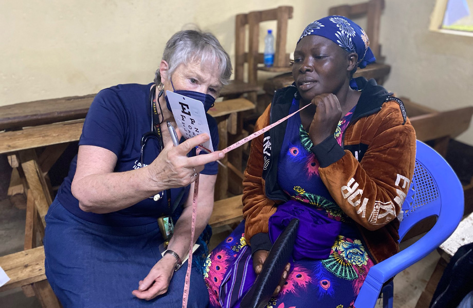 Nurse practitioner holds card with letters to test sight of Kenyan woman who holds a tape measure in her hand while reading off the card