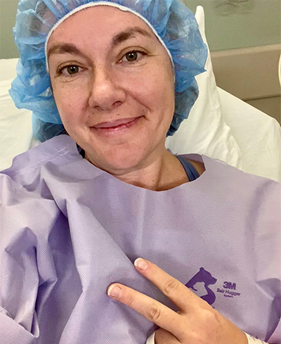 A woman in a purple hospital gown and blue cap in a hospital bed