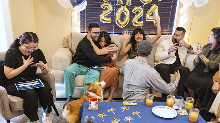 Seven people including some medical students, sit on and around a sofa celebrating Match Day results with each other