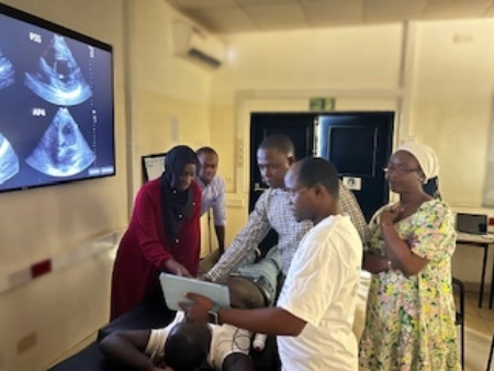 Group of people standing around patient laying on hospital bed looking at their stomach on an ultrasound screen.