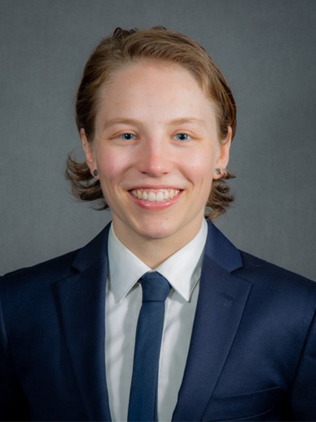 Portrait of person wearing navy blue suit jacket, white collared shirt and blue tie