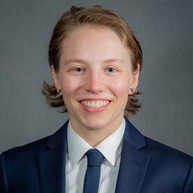 Portrait of person wearing navy blue suit jacket, white collared shirt and blue tie