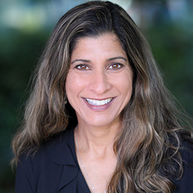 A woman with long, dark hair, wearing a black, long-sleeved blouse, smiles for a portrait.