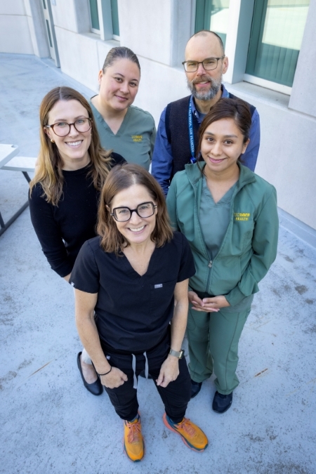 A group of four women and one man stand on an outdoor terrace looking up at the camera. 