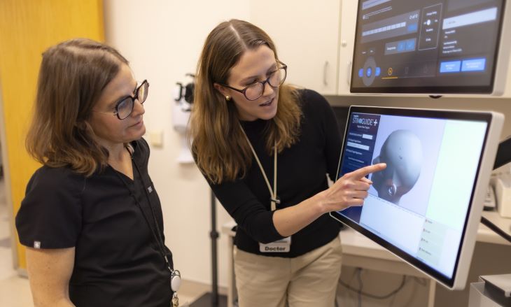 Two physicians look at a computer monitor with an image of a human head.