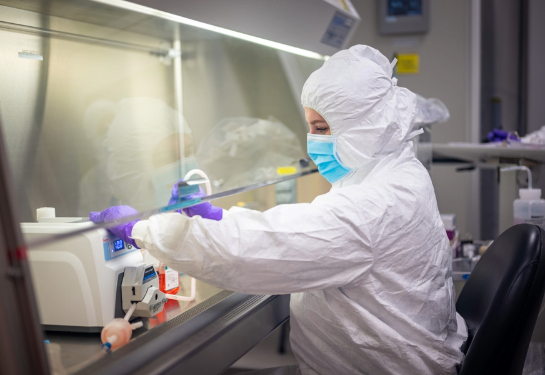 Person sitting in white surgical suit and purple glove while cycling cells through machine.  