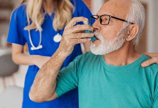 Man breathing medication from inhaler and as nurse stands behind him