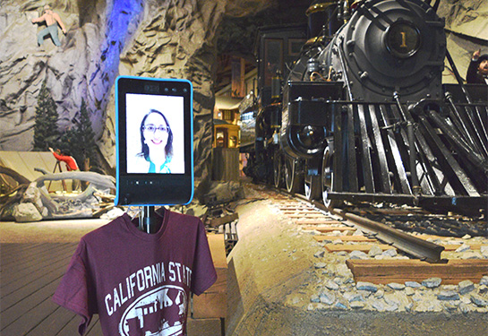 Woman walks next to two-wheeled robot with a video screen in museum.  