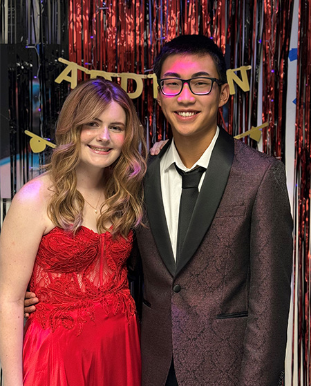 A girl wearing a red strapless gown stands next to a boy in a dark suit.