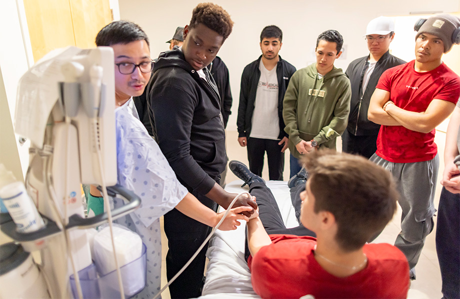 A resident shows a student how to move a device onto the wrist of another student.