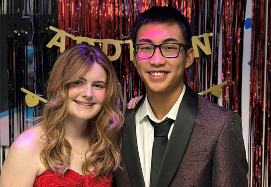 A girl wearing a red strapless gown stands next to a boy in a dark suit.