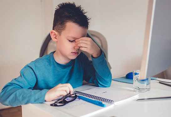 Un niño sentado frente a una computadora tocando su nariz con los dedos de su mano derecha