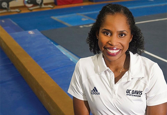 Marcia Faustin leaning on a balance beam in a gym