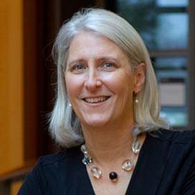 A woman with blond hair wearing a black shirt and necklace with black and clear beads smiles for a portrait. 