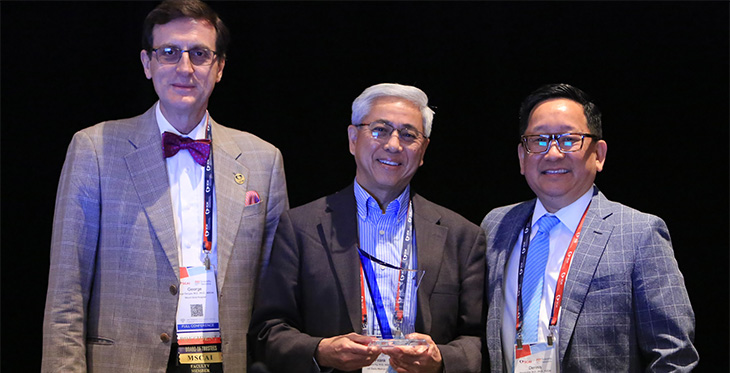 3 men stand in a row with one in the middle holding glass award.