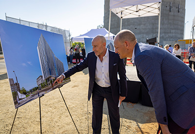 Two men leaning over looking at picture of glass building on an easel. 