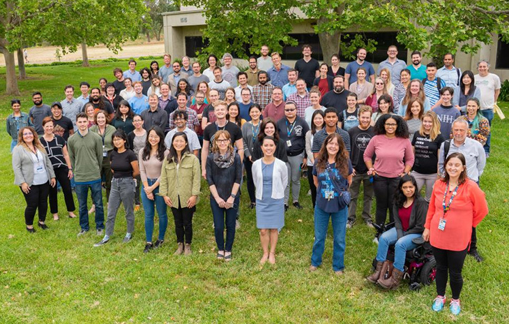 A group of people stand on a lawn in a group shot. 